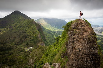 Hiker standing on rocky mountain peak overlooking lush green valley