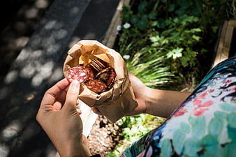 Hands holding paper bag of salami and crackers outdoors