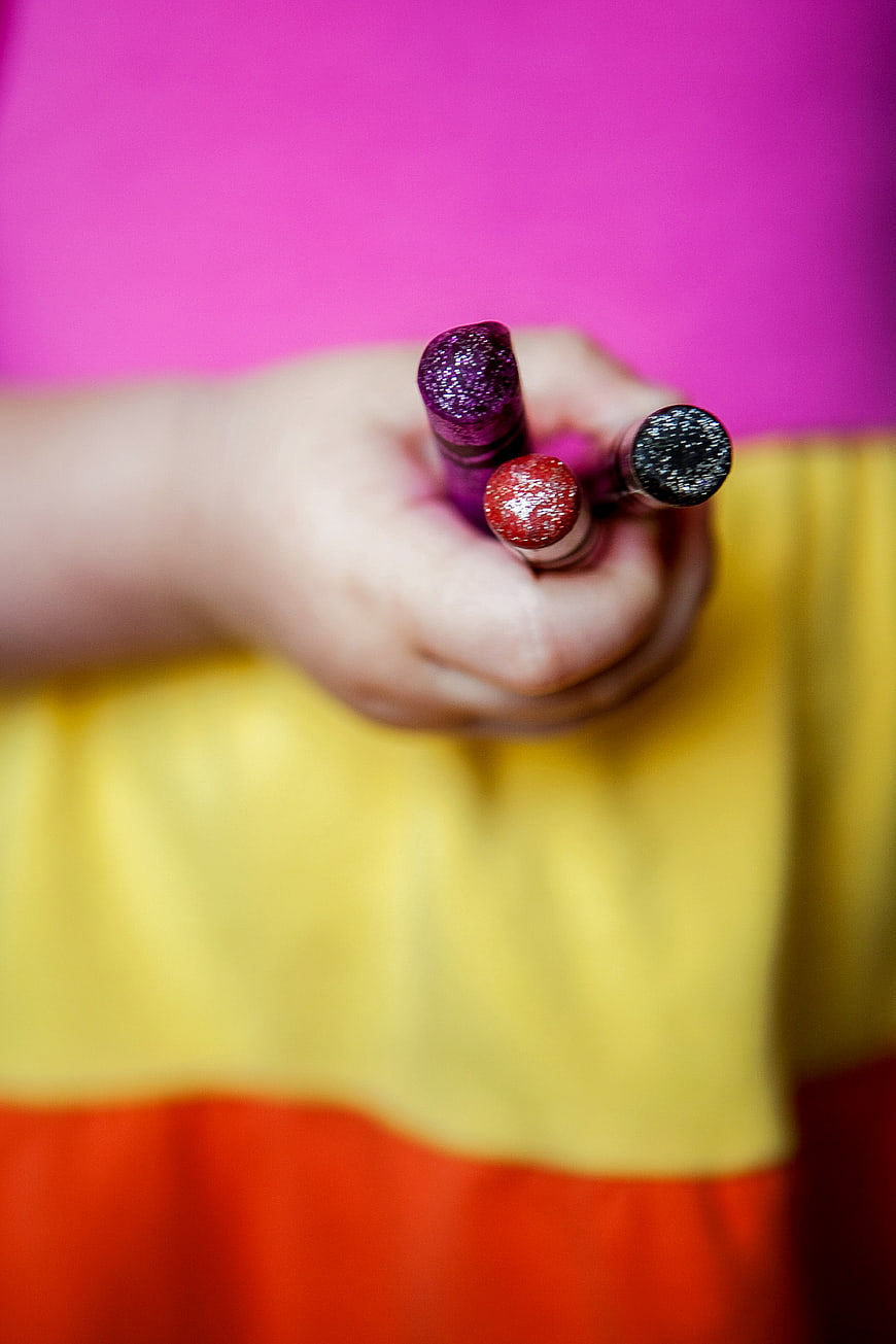 Child Holding Glittery Crayons Against Colorful Background