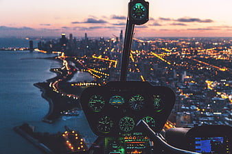 Helicopter cockpit view over city skyline at dusk