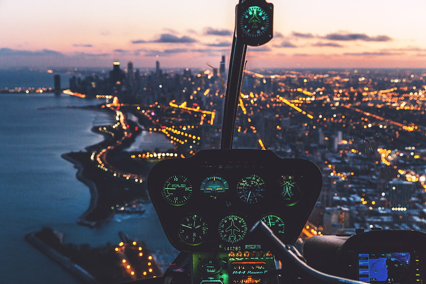 Helicopter cockpit view over city skyline at dusk