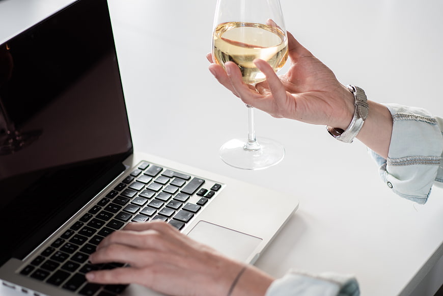 Woman drinking white wine while working on laptop