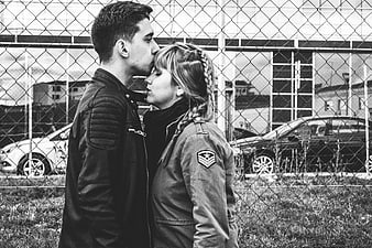 Couple kissing in front of chain link fence black and white