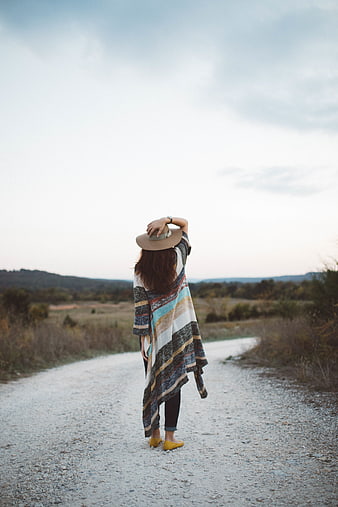Woman in poncho and hat walking on rural gravel road