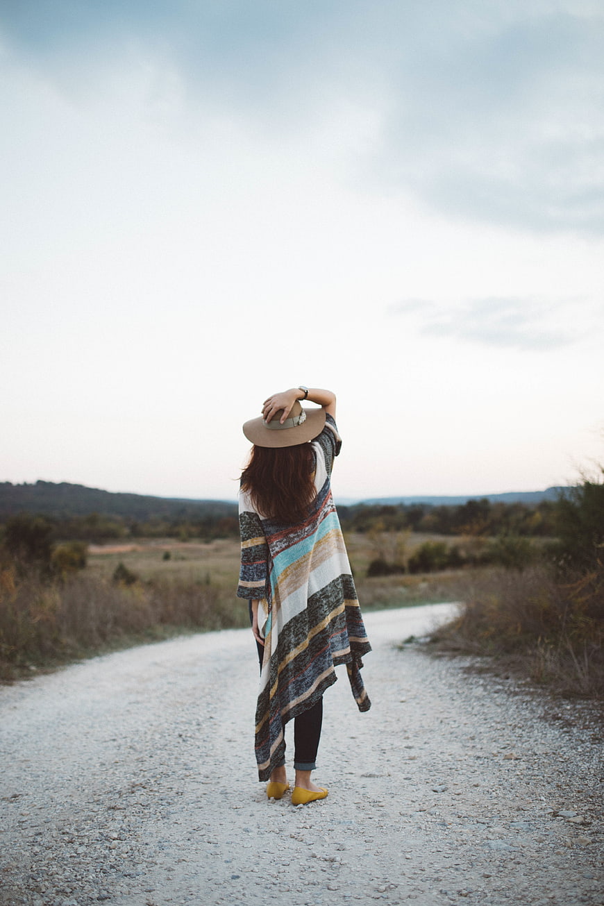 Woman in poncho and hat walking on rural gravel road