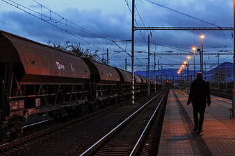 Man Walking on Train Platform at Dusk with Freight Train