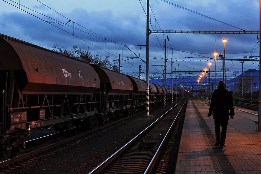Man Walking on Train Platform at Dusk with Freight Train