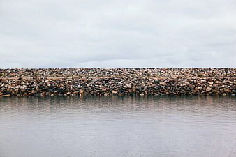 Rocky breakwater wall against calm water and overcast sky
