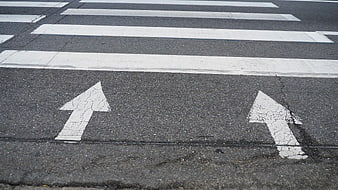 Worn white directional arrows and crosswalk stripes on asphalt road surface