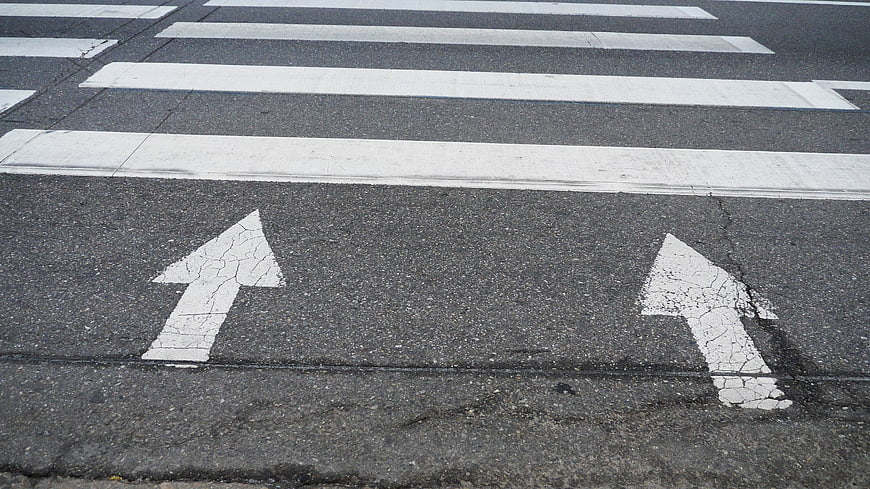 Worn white directional arrows and crosswalk stripes on asphalt road surface