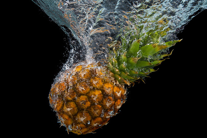 Fresh pineapple splashing into water on black background
