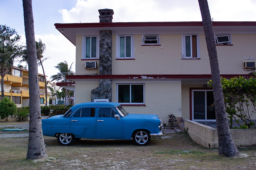 Blue vintage classic car parked in front of a house with palm trees