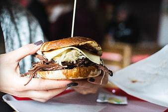 Close-up of hands holding a pulled pork sandwich with cheese