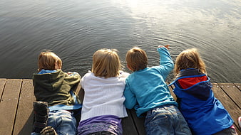 Four children lying on wooden dock looking at lake water