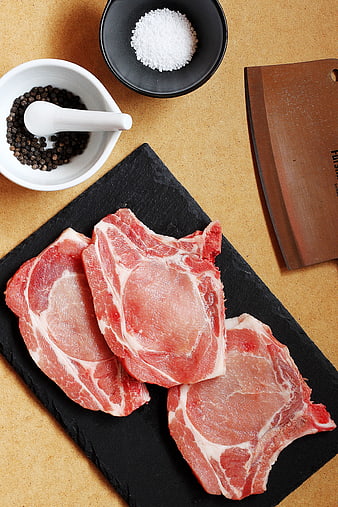 Raw pork chops on slate with salt, pepper, and cleaver