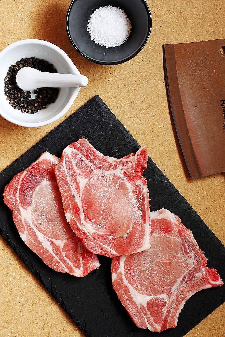 Raw pork chops on slate with salt, pepper, and cleaver