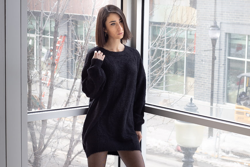 Woman in black sweater dress standing by window