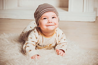 Cute baby boy smiling on fluffy rug wearing striped hat