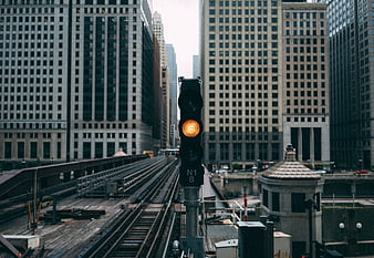Yellow railway signal light on urban train tracks between skyscrapers