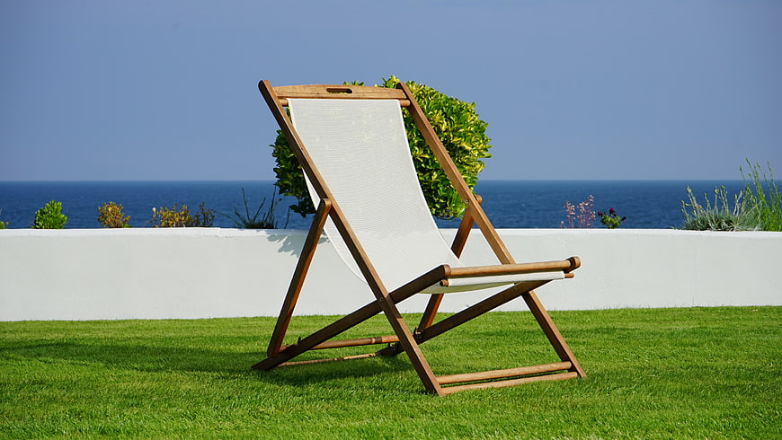 Wooden deck chair on green lawn with sea view