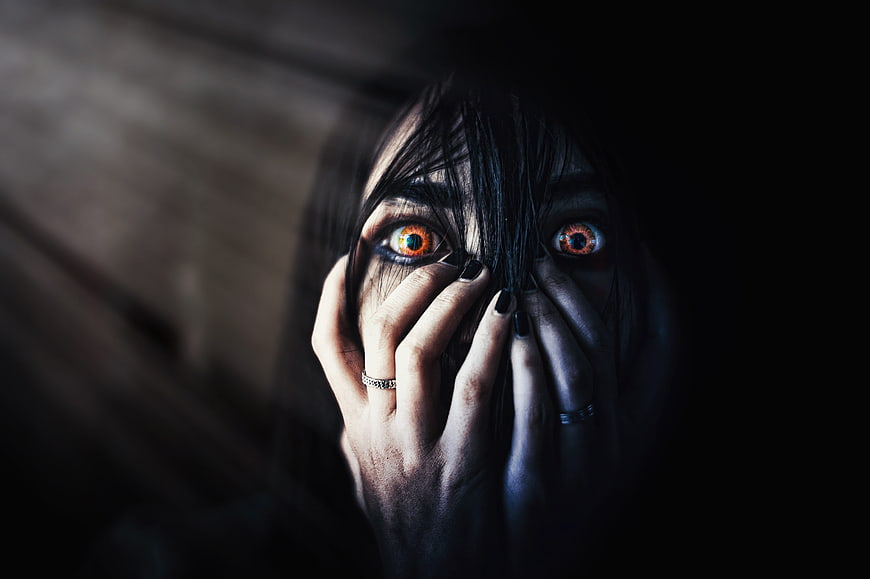 Scary woman with glowing orange eyes and hands on face