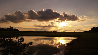 Golden sunset over pond with dramatic cloud reflections