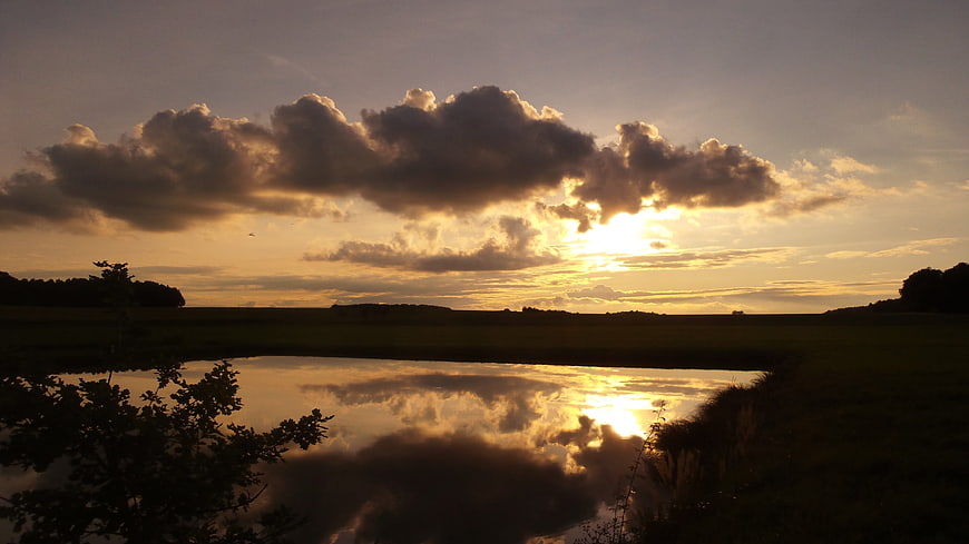 Golden sunset over pond with dramatic cloud reflections