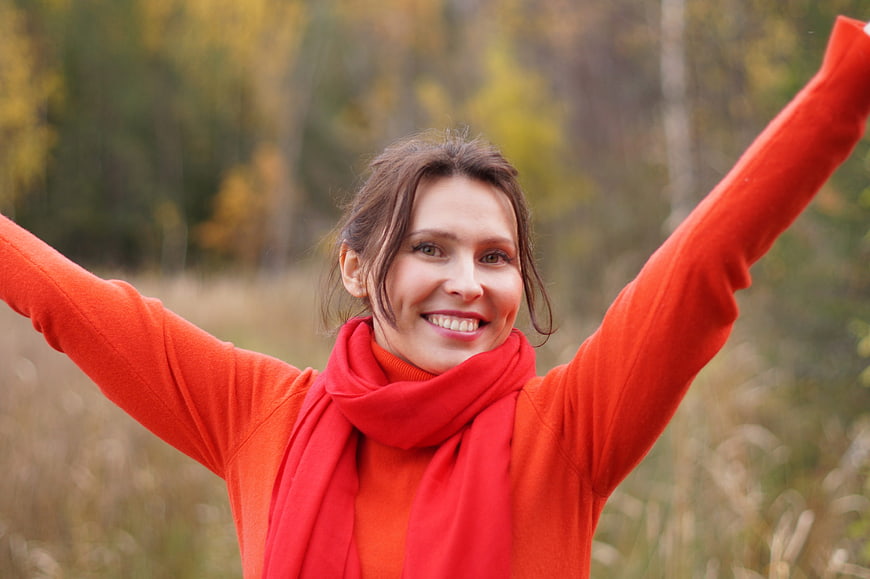 Happy Woman in Red Sweater with Arms Raised in Autumn Forest