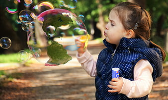 Little girl blowing soap bubble with Earth reflection in park