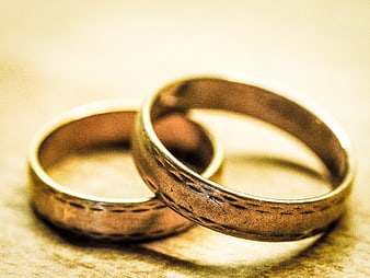 Two Textured Gold Wedding Rings Interlocked on a Warm Surface