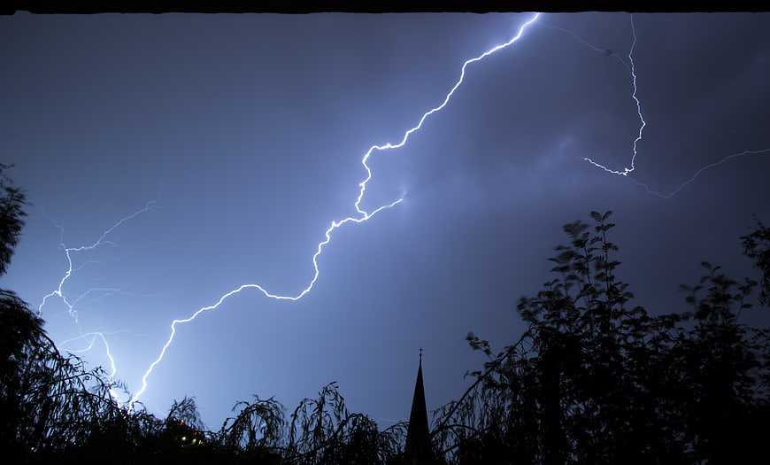 Dramatic Lightning Strike Over Silhouetted Trees and Church Spire