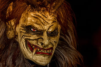 Close-up of a menacing Krampus mask with glowing red eyes and fangs