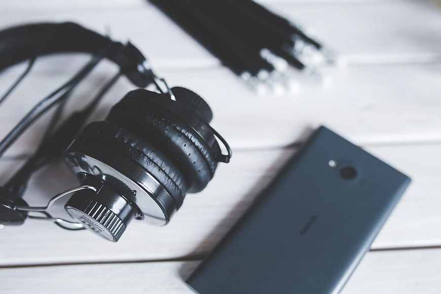 Black headphones and smartphone on white wooden table