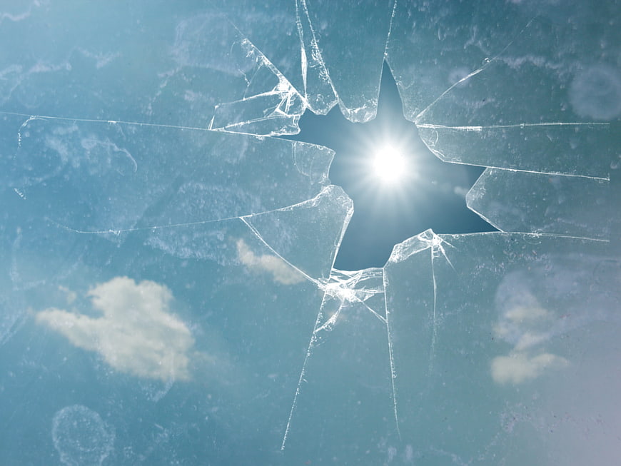 Shattered glass with sunburst against blue sky background