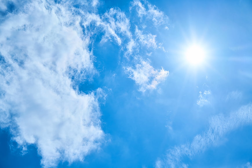 Bright Sun Shining Through Fluffy White Clouds in Blue Sky