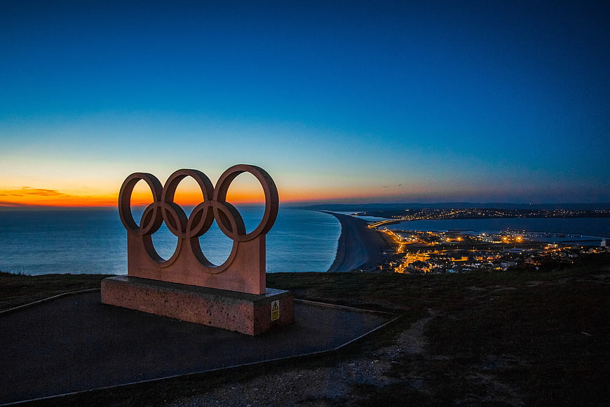 Olympic Rings Sculpture at Sunset Over Coastal City