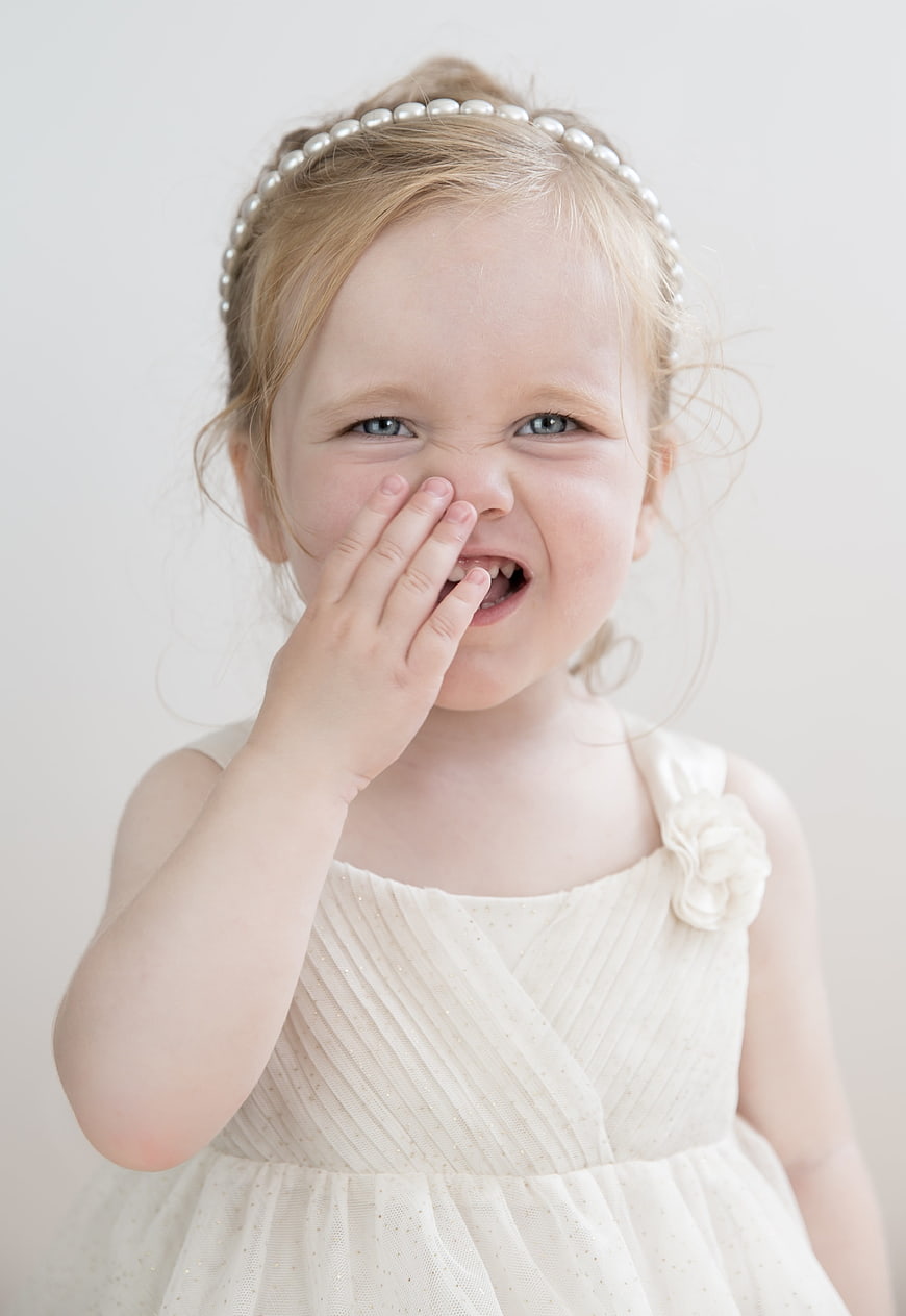 Laughing toddler girl with pearl headband covering mouth