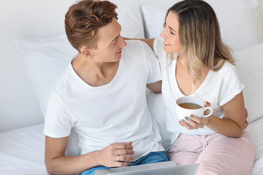 Happy young couple relaxing in bed with laptop and coffee