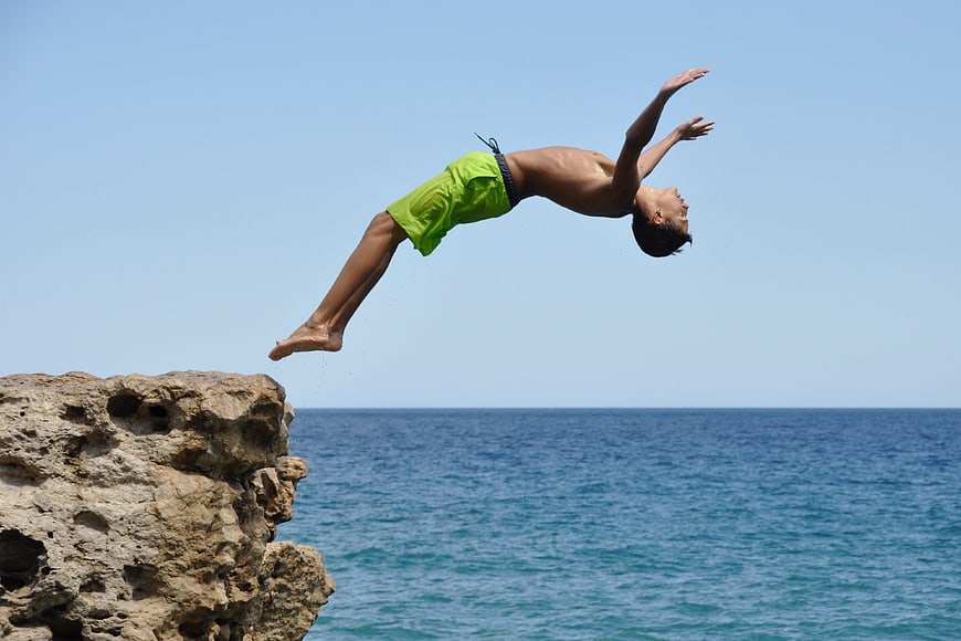 Young man performing a backflip off a coastal rock into the ocean