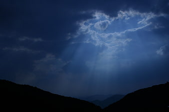 Dramatic blue sky with sun rays breaking through clouds over mountains