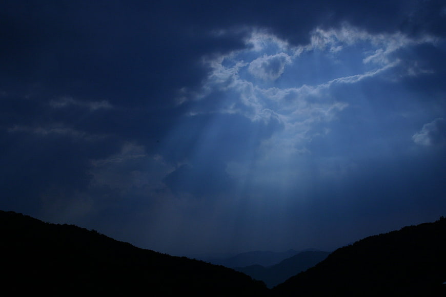 Dramatic blue sky with sun rays breaking through clouds over mountains