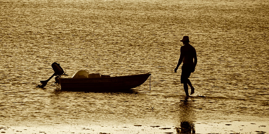Silhouette of Fisherman Walking in Water Near Boat