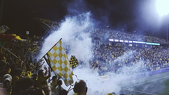 Soccer fans celebrating with smoke flares and flags in stadium