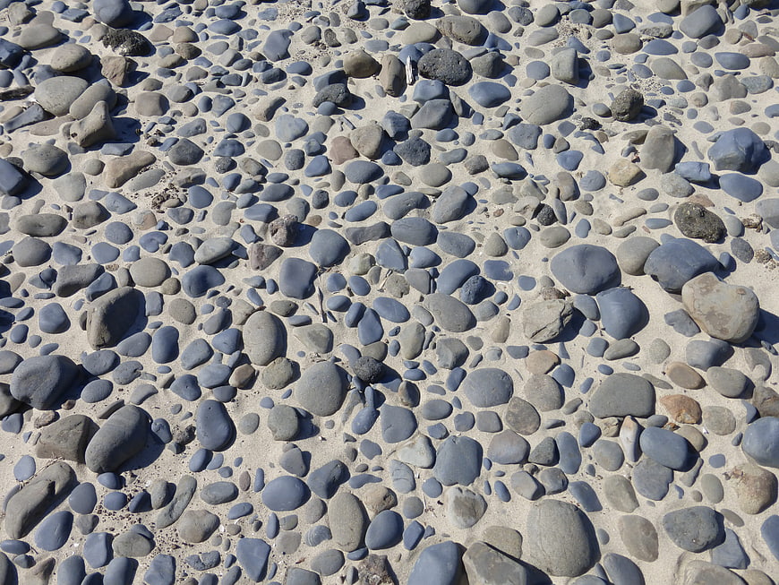 Gray pebbles and stones on sandy beach texture