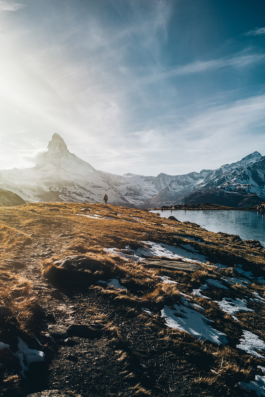 Hiker on Alpine Meadow with Snowy Mountain Peak and Lake