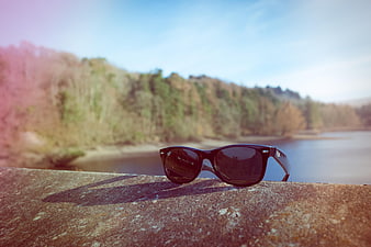 Black Sunglasses Resting On Concrete Railing By Lake