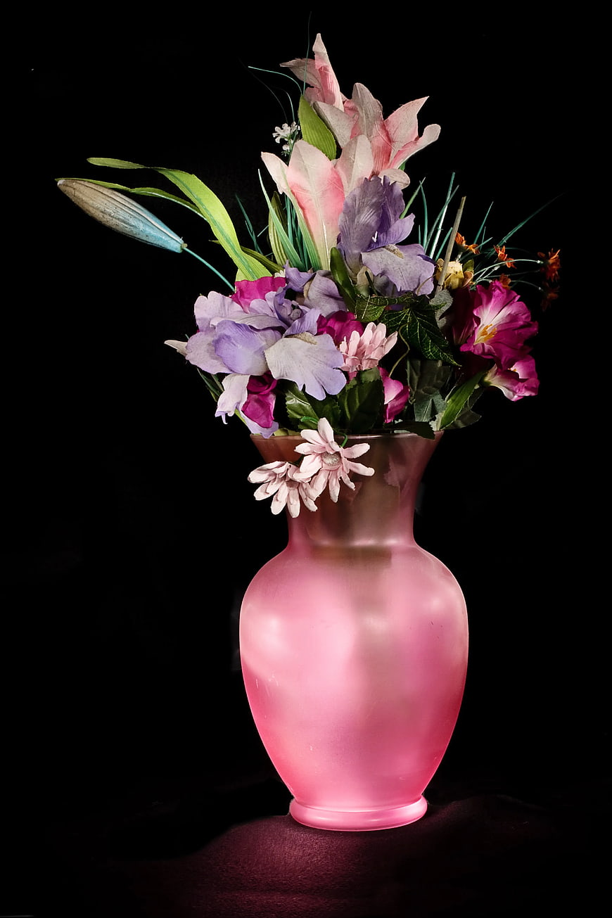 Pink frosted vase with colorful artificial flowers on black background