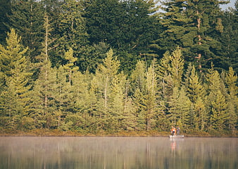 Two people fishing from a boat on a calm lake surrounded by forest