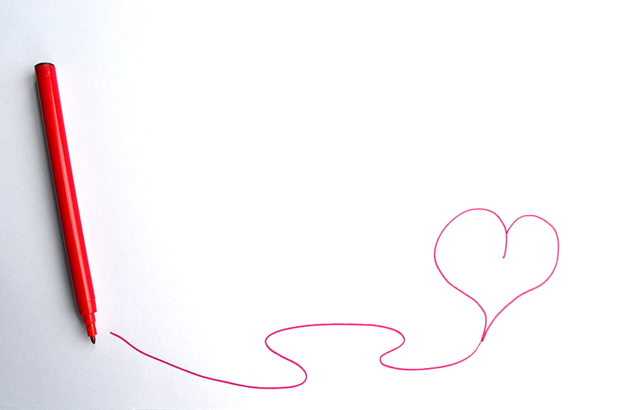 Red marker drawing a continuous line into a heart shape on white paper