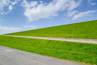 Green grassy dike with path under blue sky